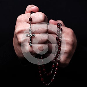 Female hands praying holding a rosary with Jesus Christ in the cross or Crucifix on black background.