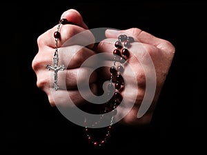 Female hands praying holding a rosary with Jesus Christ in the cross or Crucifix on black background