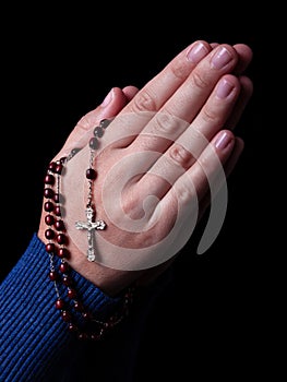 Female hands praying holding a rosary with Jesus Christ in the cross or Crucifix on black background.