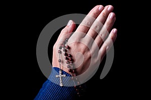 Female hands praying holding a rosary with Jesus Christ in the cross or Crucifix on black background.