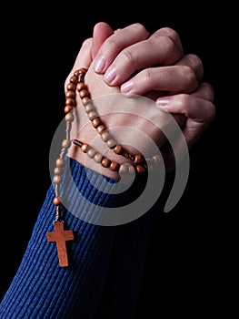 Female hands praying holding a rosary with Jesus Christ in the cross or Crucifix on black background.