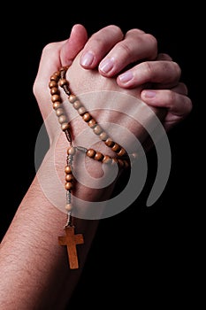 Female hands praying holding a rosary with Jesus Christ in the cross or Crucifix on black background.