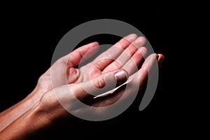 Female hands praying with palms up arms outstretched. Black background photo