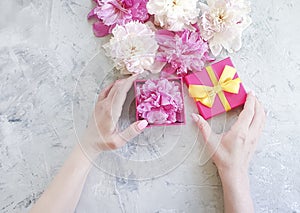 Female hands present  holding a peony flower gift box on a gray concrete background