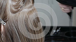 Female hands of a professional hairdresser dry hair with a hairdryer and do styling in a hairdressing salon.