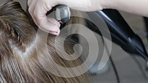 Female hands of a professional hairdresser dry hair with a hairdryer and do styling in a hairdressing salon.