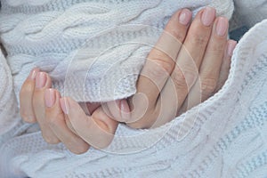 Female hands with professional natural manicure on short nails on the background of a knitted white woolen scarf. Hand care,