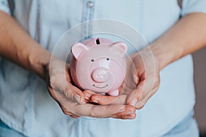 Female hands protect pink piggy bank, copy space. Concept of saving money or savings