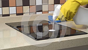 Female hands in protective gloves cleaning the surface of an induction cooker.