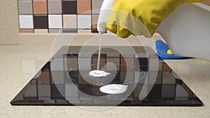 Female hands in protective gloves cleaning the surface of an induction cooker.