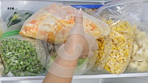 Female Hands pulls frozen Bell pepper out of the fridge. Frozen fruits, vegetables, meat in the freezer.