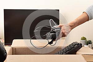 Female hands put old keyboard and chargers in box with old used computers and gadget devices for recycling. Planned