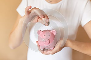 Female hands puts a coin in a pink piggy bank. The concept of saving money or savings, investment