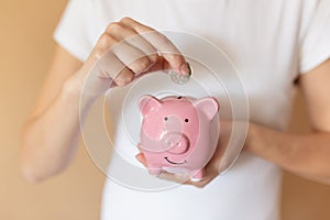 Female hands puts a coin in a pink piggy bank. The concept of saving money or savings, investment