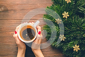 Female hands with red manicure holding a cup of tea on a background of Christmas decorations