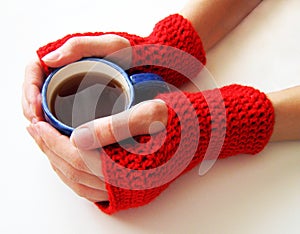 Female hands in red mittens are holding a cup of hot drink