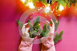 Female hands with red nails, branches of christmas fir tree, magic lights and pieces of golden paper on red table. Christmas decor