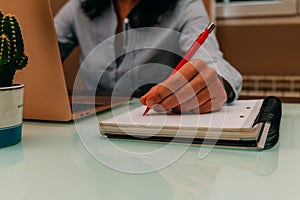 Female hands with a red pen writing on notebook. Selective focus