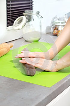 Female hands roll the dough for baking on a green silicone coffee table lying on the kitchen counter.