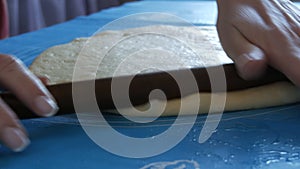 Female hands roll out the dough with a rolling pin on a special silicone mat for kneading the dough. Modern technology