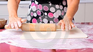 Female hands roll out the dough with a rolling pin on a wooden surface, close-up. female hands rolling dough on a lilac