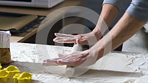 Female hands roll out dough with rolling-pin on wooden table covered in flour