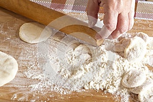 Female hands roll out the dough with a wooden rolling pin on a board with flour.