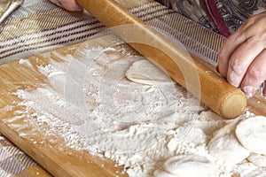 Female hands roll out the dough with a wooden rolling pin on a board with flour.