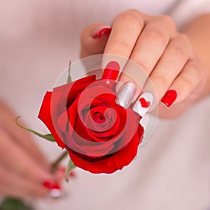 Female hands with romantic manicure nails, hearts design, holding red rose