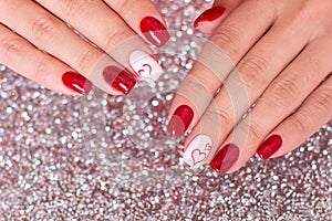 Female hands with romantic manicure, red gel polish, hearts on nails