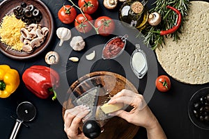 Female hands rubbed cheese grated on pizza, ingredients for cooking pizza on black table, top view