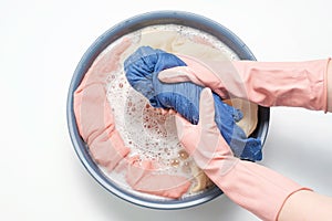 Female hands in rubber gloves wring out blue clothes on background of a basin close-up, top view.