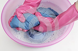 Female hands in rubber gloves wring out blue clothes on a background of a basin with linen close-up, top view