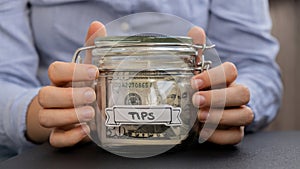 Female hands Saving Money In Glass Jar filled with Dollars banknotes. TIPS transcription in front of jar. Managing