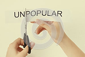 Female hands scissor the word unpopular photo