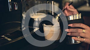 Female Hands Scooping Frothed Milk On Top Of Warm Coffee In The Office. close up