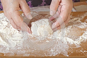 Female hands sculpt a bunch of raw dough on a wooden board with flour.