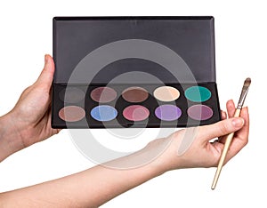 In female hands a set of colorful eye shadow and cosmetic brush