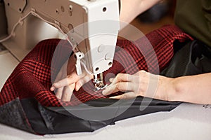 Female hands at sewing process and repairing plaid fabric on professional manufacturing machine. Close up view.