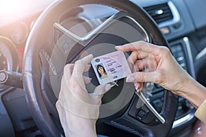 Female hands show US driving license, against the background of a car steering wheel