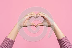 Female hands showing a heart shape isolated on a color light pink background. Sign of love, harmony, gratitude, charity. Feelings