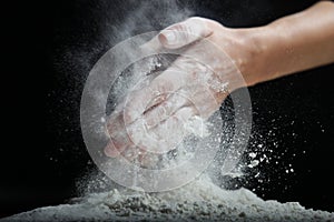 Female hands sift flour with a metal sieve on a black background.
