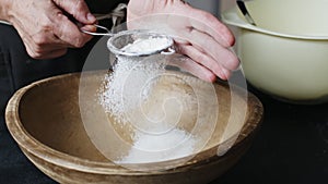 Female hands sifting flour by bowl.