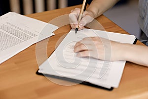 Female hands signing documents, wooden table in office.