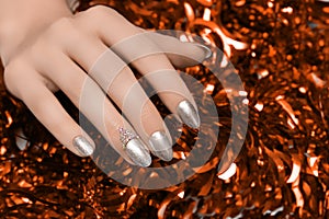 Female hands with silver Christmas nail design. Silver nail polish manicured hands. Female holding red New Year tinsel