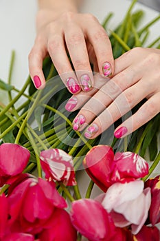 Female hands with spring manicure and tulips nail art, floral design on flowers background. Beauty, fingernails and hands care