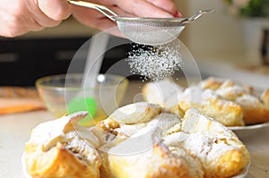 Female hands sprinkle powdered sugar on apple puffs