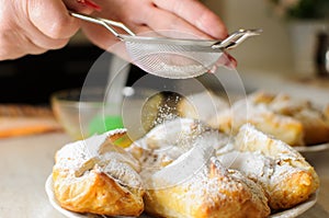 Female hands sprinkle powdered sugar on apple puffs