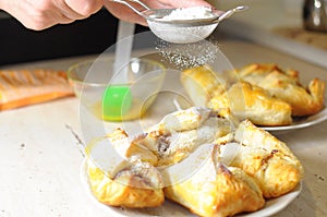 Female hands sprinkle powdered sugar on apple puffs