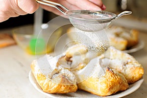 Female hands sprinkle powdered sugar on apple puffs